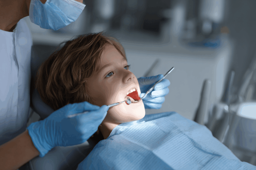 Petit enfant allongé sur un fauteuil de dentiste ouvrant la bouche pendant un contrôle dentaire simple, dentiste utilisant un miroir dentaire, environnement propre et moderne, ambiance calme et rassurante, lumière naturelle, photographie réaliste, style magazine santé.