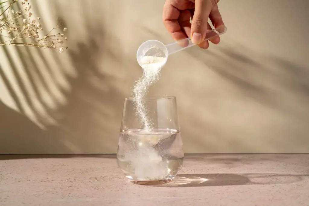 Photo d'un grand verre d'eau posé à côté d'une poudre de collagène marin avec une cuillère doseuse, ambiance hydratation et santé.