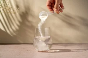 Photo d'un grand verre d'eau posé à côté d'une poudre de collagène marin avec une cuillère doseuse, ambiance hydratation et santé.